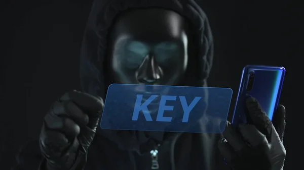 Hacker con máscara negra saca la pestaña CLAVE de un teléfono inteligente. Concepto de hackeo — Foto de Stock