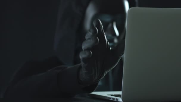 Hacker con máscara negra tira de la pestaña clave de un ordenador portátil — Vídeo de stock