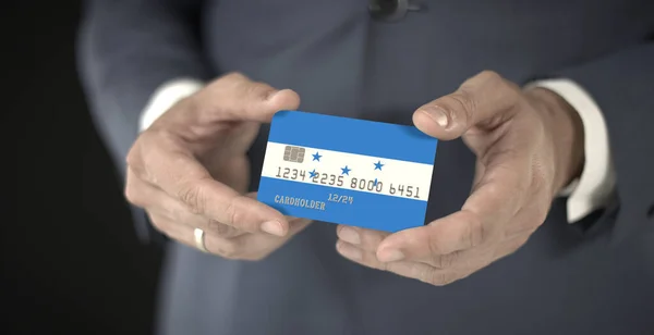 Επιχειρηματίας κατέχει πιστωτική κάρτα με τυπωμένη σημαία της Ονδούρας στα χέρια του, φανταστικούς αριθμούς — Φωτογραφία Αρχείου