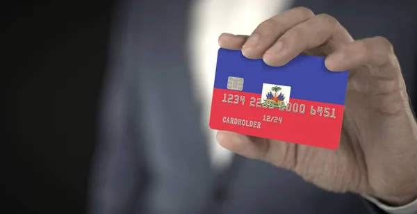 Empresário segura cartão bancário com bandeira impressa do Haiti em sua mão, números fictícios — Fotografia de Stock