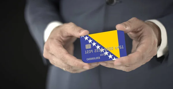 Un homme tient dans ses mains une carte bancaire en plastique avec le drapeau de Bosnie-Herzégovine, des numéros fictifs — Photo