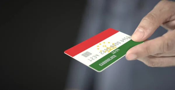 Man gives credit card with printed flag of Tajikistan. Fictional numbers — Stock Photo, Image
