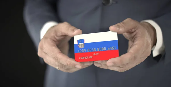 商人手里拿着印有斯洛文尼亚国旗的信用卡，上面有虚构的数字 — 图库照片