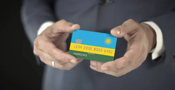 Επιχειρηματίας κατέχει πλαστική τραπεζική κάρτα με τυπωμένη σημαία της Ρουάντα στα χέρια του, φανταστικούς αριθμούς — Φωτογραφία Αρχείου