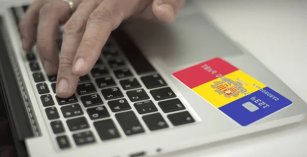 Homme paie en ligne avec une carte bancaire en plastique avec le drapeau imprimé d'Andorre. Numéros fictifs — Photo