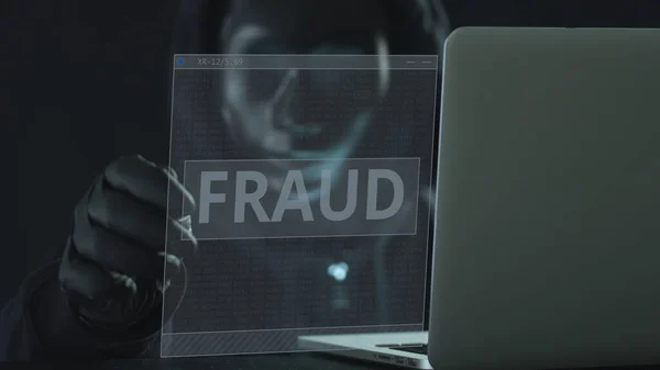 Hacker usando máscara preta puxa guia FRAUD de um laptop — Fotografia de Stock