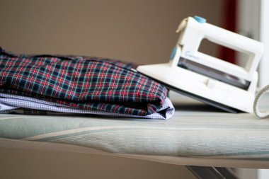 Evdeki masa ütülemesi için bir yığın gömlek ve elektrikli ütü. Ev kavramı.