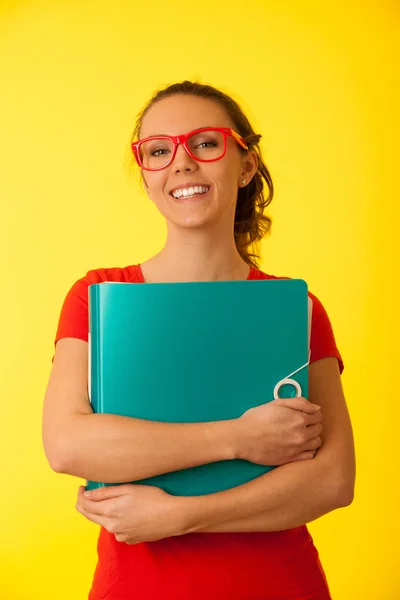 シャツで美しい若い女性学生が黄色の背景上フォルダーを保持します — ストック写真