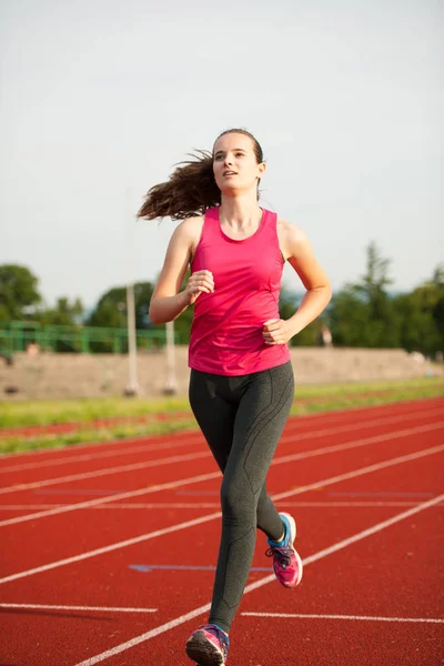 一个美丽的年轻女子赛跑选手在夏初的下午在跑道上跑步 — 图库照片