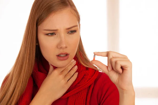 Wanita muda bersweater merah memegang pil di tangannya saat dia sakit. — Stok Foto