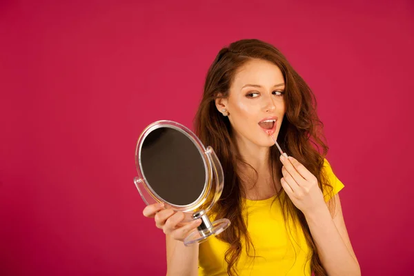 Atractiva mujer joven aplicando brillo de labios mirando en el espejo sobre —  Fotos de Stock