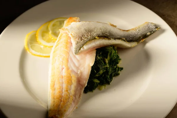 Roasted fish filet decorated with lemon slices on a plate