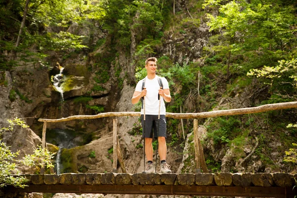 Hombre activo descansando en un puente sobre el arroyo de montaña —  Fotos de Stock