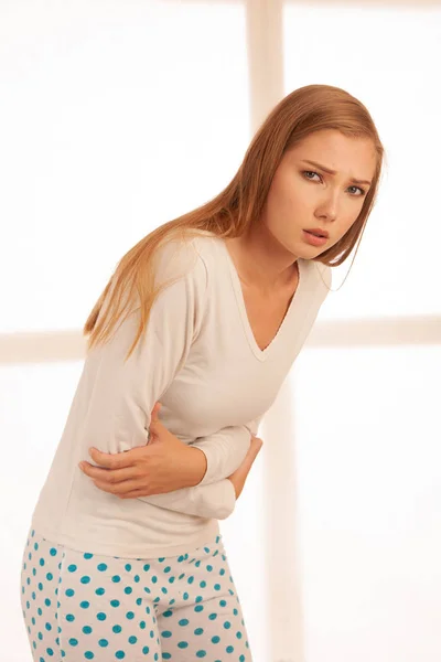 Jeune femme souffrant de douleurs abdominales tout en étant assis sur le lit un — Photo