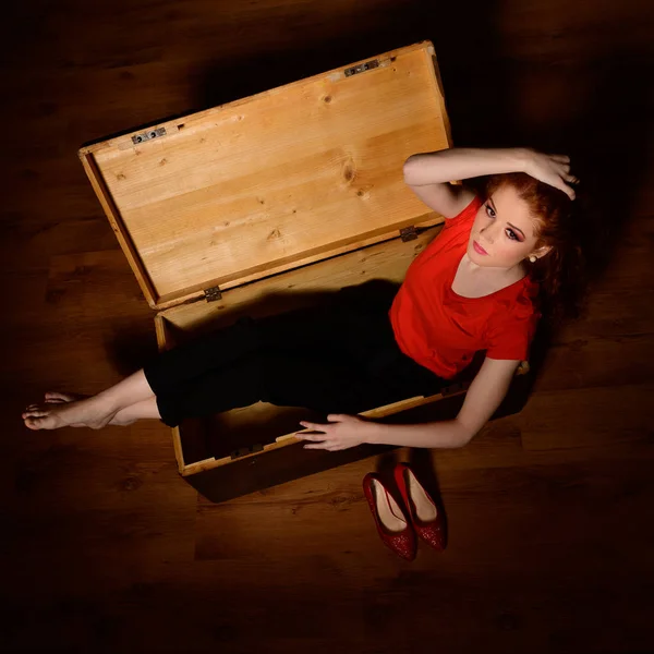 Güzel kızıl saçlı kadın eski tahta bir sandıkta oturuyor. — Stok fotoğraf