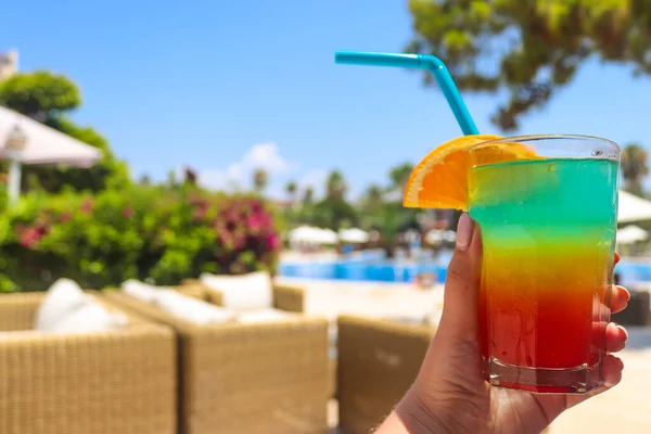 Fresh juicy tropical cocktail in woman\'s / girl\'s hand near the pool. Colorful cocktail, cold drink. Summer concept. Beach vacation and traveling concept. Copy space for text. Close-up