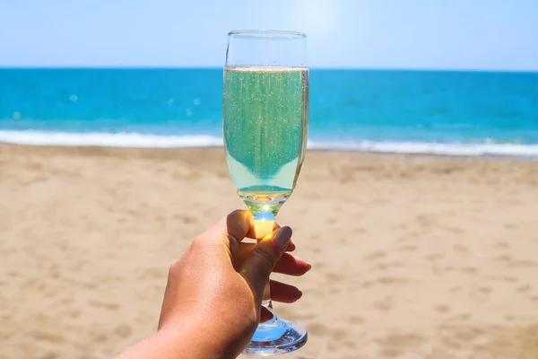 A glass of sparkling wine or champagne in a woman\'s hand against the backdrop of a seascape. Relax and vacation concept. Close-up