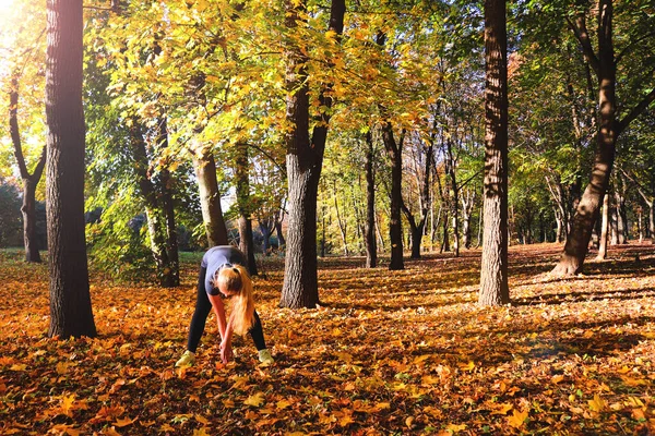 Young caucasian woman doing fitness exercise in nature in the autumn park. Sports and outdoor activities. Autumn mood. Copy spase, selective focus.