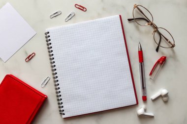 Eğitim ya da iş için çalışma alanı. Not defteri, kadın gözlükleri, kablosuz kulaklıkları mermer arka planda kalem ve kağıt tokaları olan farklı ofis malzemeleri.