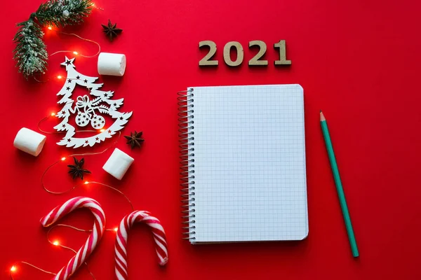 Noel süslemeleri ve parlak kırmızı arka planda yılın hedefleri ya da sonuçları için not defteri. Yeni yıl hedef listesi 2021. Üst manzara, düz yatış. Şenlikli ve tatil konsepti.