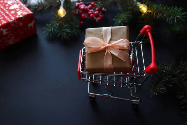 Noel alışverişi konsepti. Market arabası ve şenlik arka planında mevcut. Kış tatilleri, indirimler ve sezon satışları. Yakın plan, seçici odaklanma. Noel arkaplanı.