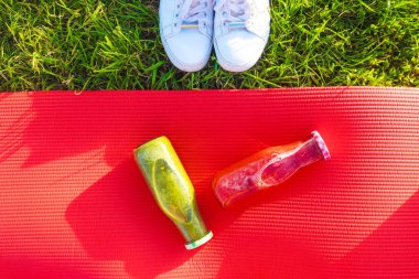 Spor ve detoks. Meyve suları çimlerin üzerinde bir spor halısının üzerinde uzanıyor. Spor malzemeleri. Sağlıklı yaşam tarzı, spor ve diyet konsepti. Boşluğu, düzlüğü, düzeni kopyala