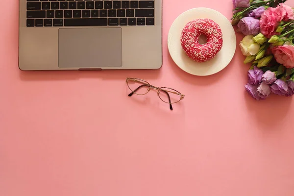 분홍색 배경에는 노트북, 도넛, 꽃, 안경이 있는 아름다운 여성 작업장이 있다. 사업, 프리랜서, 교육 개념. 위에서 본 것, 평평 한 것, 설계를 위한 복사 공간 — 스톡 사진