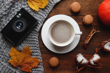 Sonbahar mahsulü kompozisyon. Bir fincan kahve, balkabağı, ekose ve pamuk dalı, eski model kamera, makaronlar, tarçın çubukları ve akçaağaç yaprakları. Sonbahar ruh hali. Üst görünüm, düz yatış, yumuşak odaklanma..
