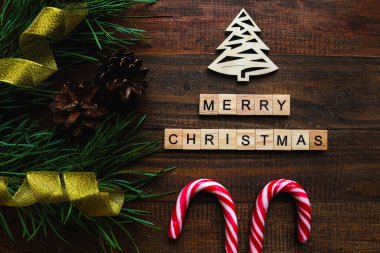 İçinde çam dalları, altın kurdele, ahşap Noel ağacı ve koyu dokuda Merry Noeli yazan ahşap harfler olan bir Noel kartı ya da arka plan. Şenlikli, tatil konsepti. Üst manzara, düz uzanma.