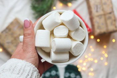 Bir kadının eli bulanık tatil geçmişinde şekerleme dolu bir fincan tutuyor. Kış, festival ve tatil konsepti. Yeni yıl ve Noel kartpostalı. Üst görünüm, seçici odak, yakın çekim, düz uzanma.