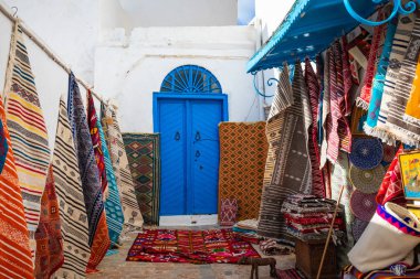 Traditional Tunesian carpets hanging on blue walls in resort town Sidi Bou Said. Tunisia, North Africa. clipart