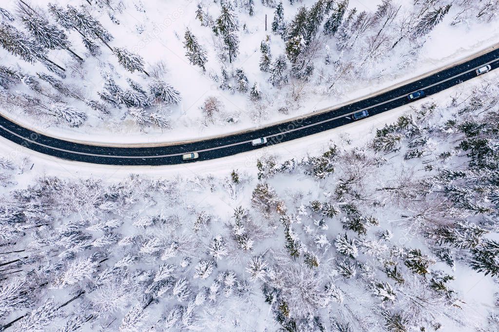 Curvy windy road in snow covered forest, top down aerial view. Winter landscape. 