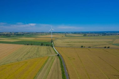 Rüzgar türbininin havadan görünüşü. Hasat zamanı yel değirmenleri, yukarıdan tarlalar. Tarım tarlaları bir yaz günü. Yenilenebilir Enerji.