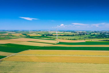 Rüzgar türbininin havadan görünüşü. Hasat zamanı yel değirmenleri, yukarıdan tarlalar. Tarım tarlaları bir yaz günü. Yenilenebilir Enerji.