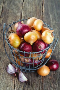 ahşap yüzey üzerinde bir demir sepet içinde kırmızı ve sarı soğan