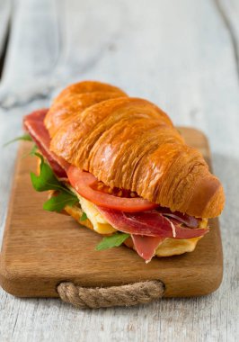 argugula, jamon, peynir ve domates ahşap yüzeyde kruvasan