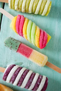 Turkuaz ahşap arka plan üzerinde renkli buzlu çubuk dondurma