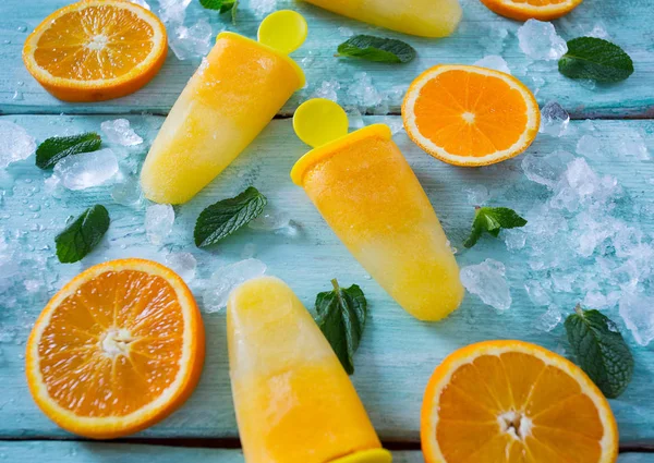 home made orange popsicles on turquoise wooden surface