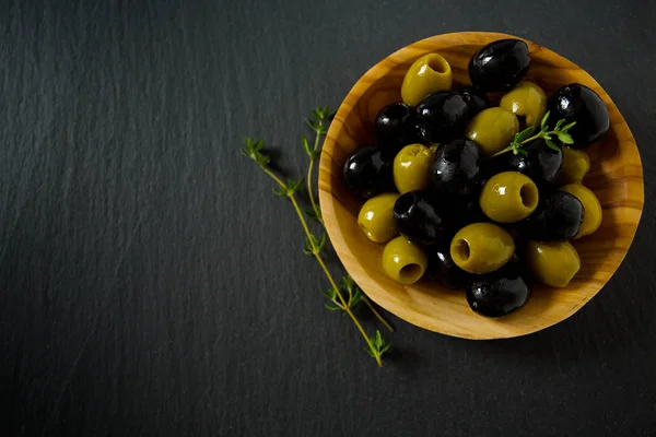 olives in a wooden bowl on black surface