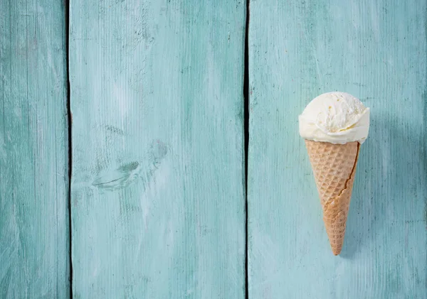 single vanilla ice cream in waffle scone on turquoise surface