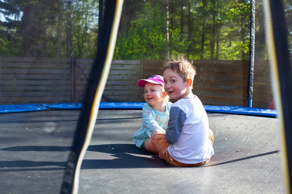 Lindos hermanos sentados en un trampolín en un día de primavera —  Fotos de Stock