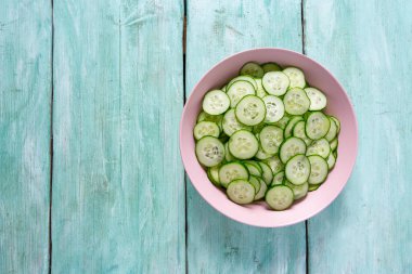 Turkuaz yüzeyinde bir kasede salatalıklar.