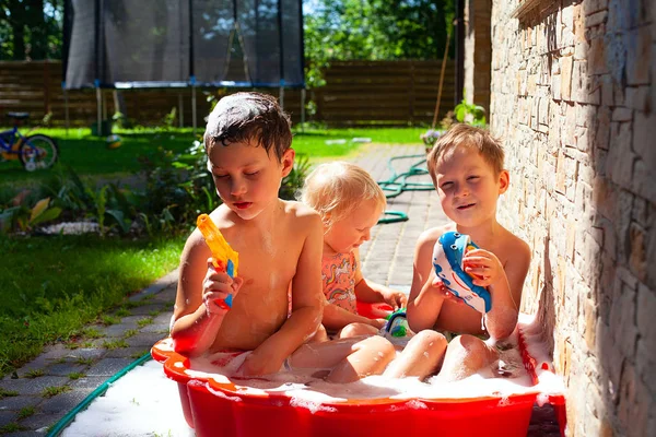 Tres niños nadando en un tirón de plástico lleno de agua de espuma —  Fotos de Stock