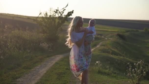 在一个阳光明媚的日子里, 带着她的小儿子在一个美丽的年轻母亲的湖面上散步. — 图库视频影像