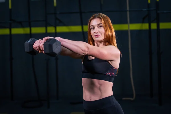 Genç, güzel, kızıl saçlı kız spor salonunda bir dambılla spor yapıyor..