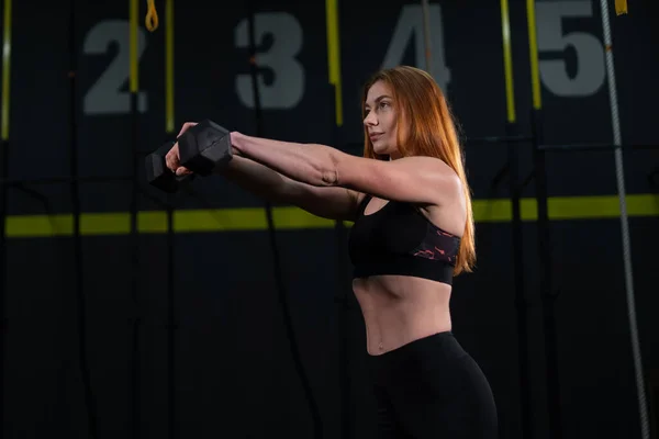 Genç, güzel, kızıl saçlı kız spor salonunda bir dambılla spor yapıyor..