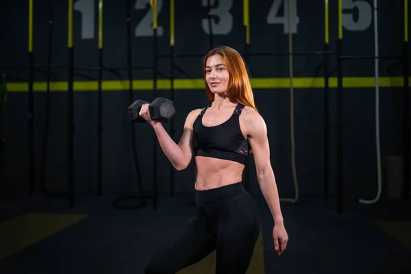 Genç, güzel, kızıl saçlı kız spor salonunda bir dambılla spor yapıyor..