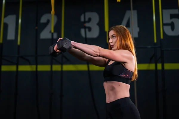 Genç, güzel, kızıl saçlı kız spor salonunda bir dambılla spor yapıyor..