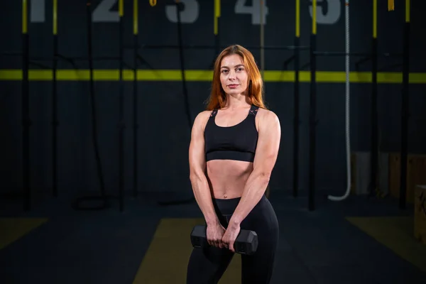 Genç, güzel, kızıl saçlı kız spor salonunda bir dambılla spor yapıyor..