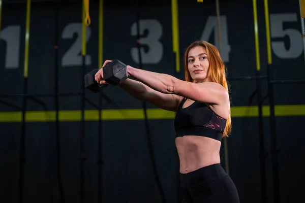 Genç, güzel, kızıl saçlı kız spor salonunda bir dambılla spor yapıyor..